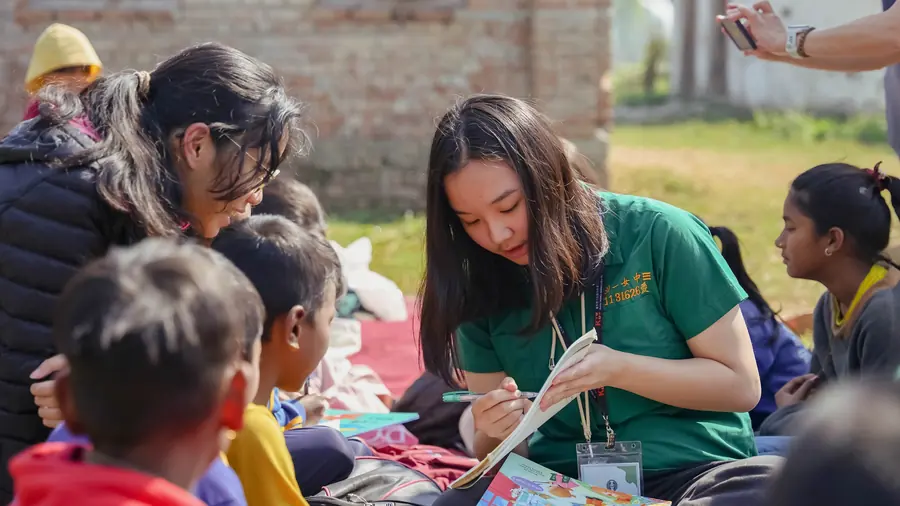 A student leading a reading session with village children, a Nepali teacher alongside
