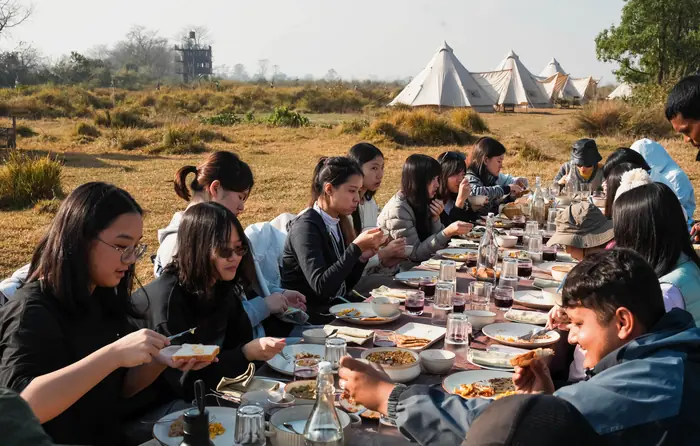Students eating breakfast at a long table in front of the tents